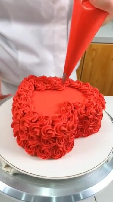 Heart-shaped cake being decorated with red buttercream roses